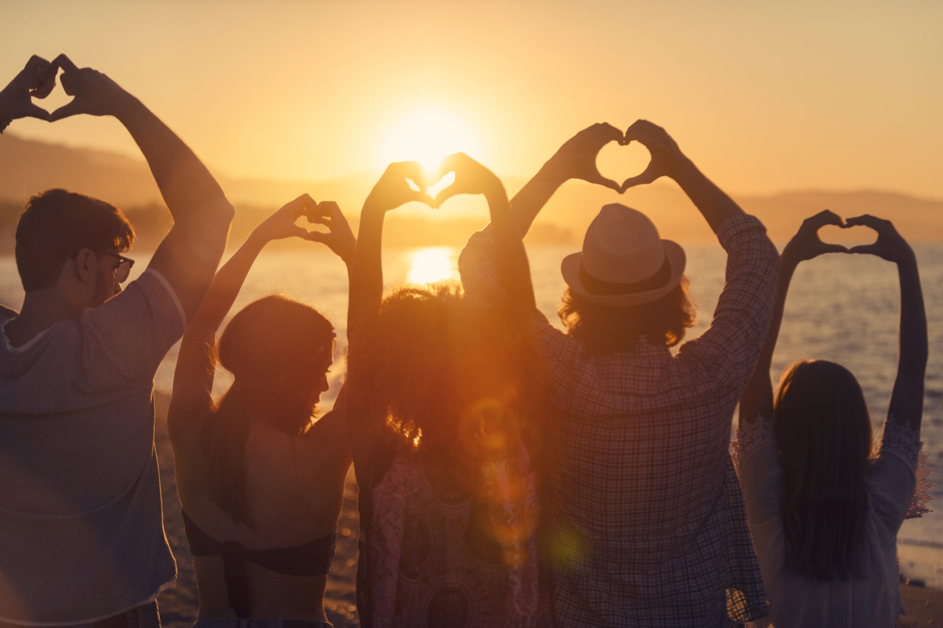 Grupo de personas haciendo señales de corazón de amor al atardecer.