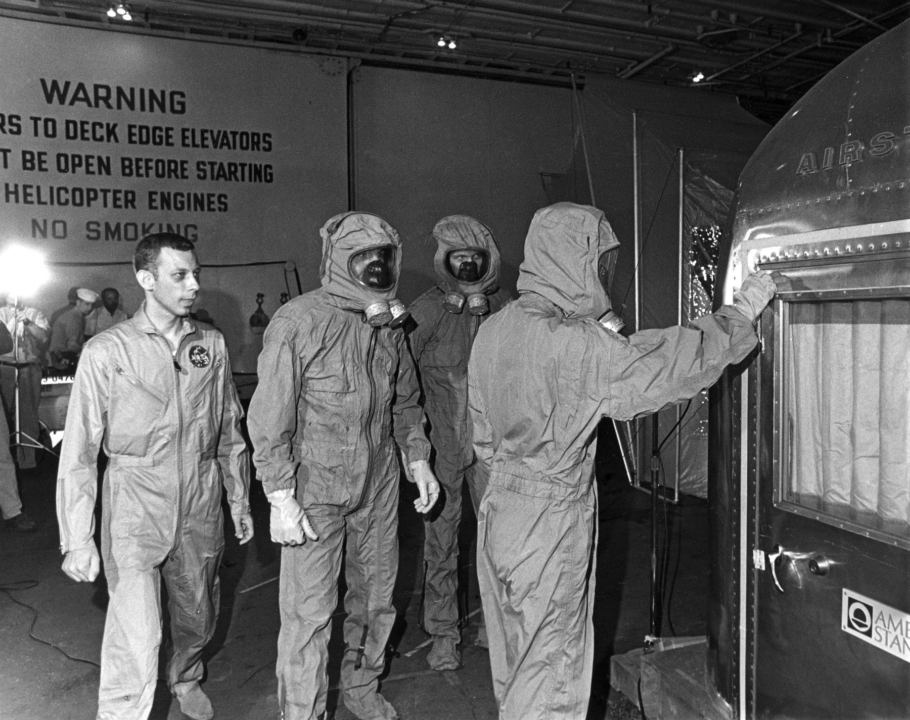 El cirujano de vuelo Dr. William R. Carpentier, izquierda, y los tres astronautas sustitutos que usan prendas de aislamiento biológico, se preparan para ingresar a la Instalación Móvil de Cuarentena (MQF) a bordo del USS Guadalcanal.