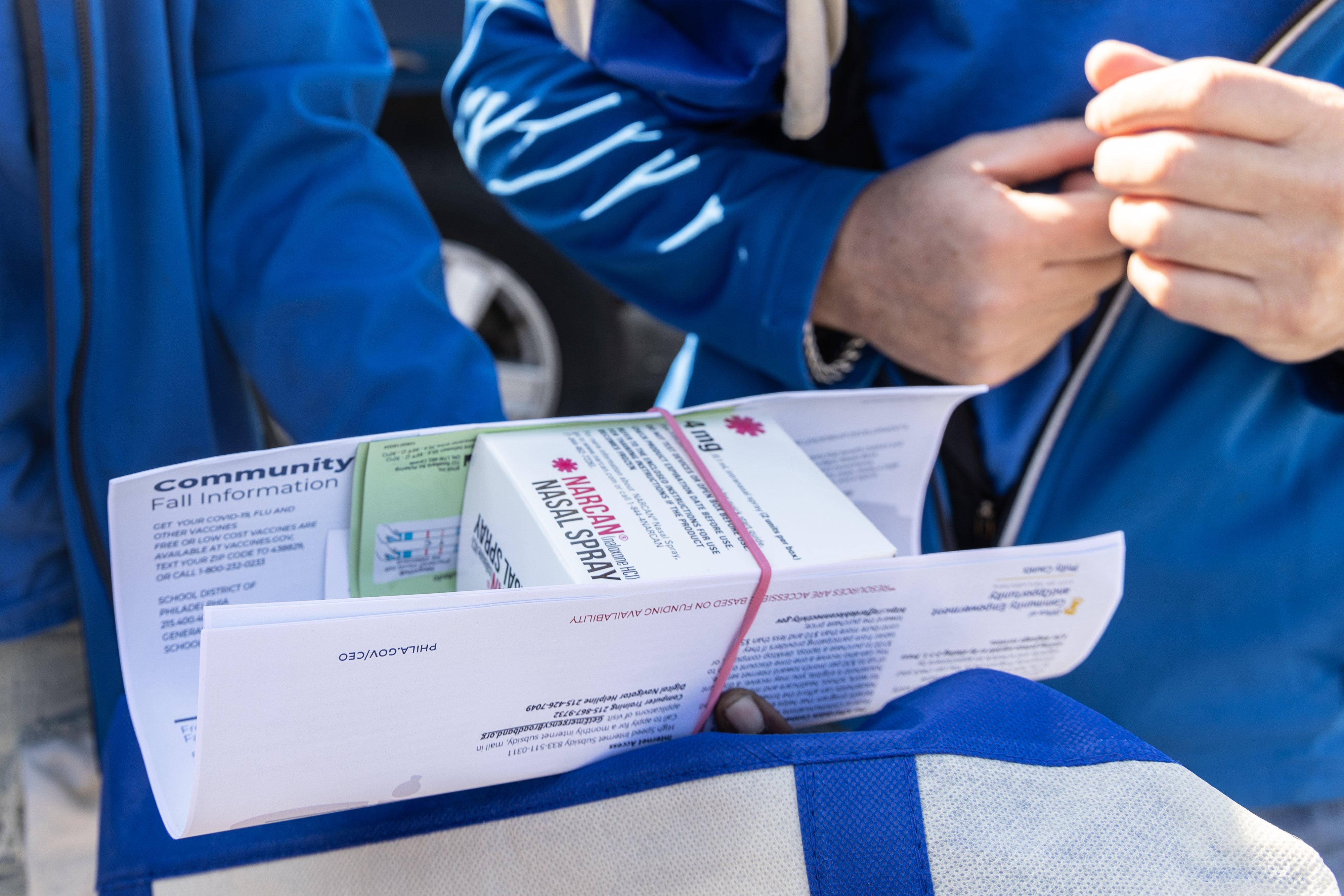 Un primer plano de una caja de Narcan y dos personas con chaquetas azules a juego sosteniendo la caja.