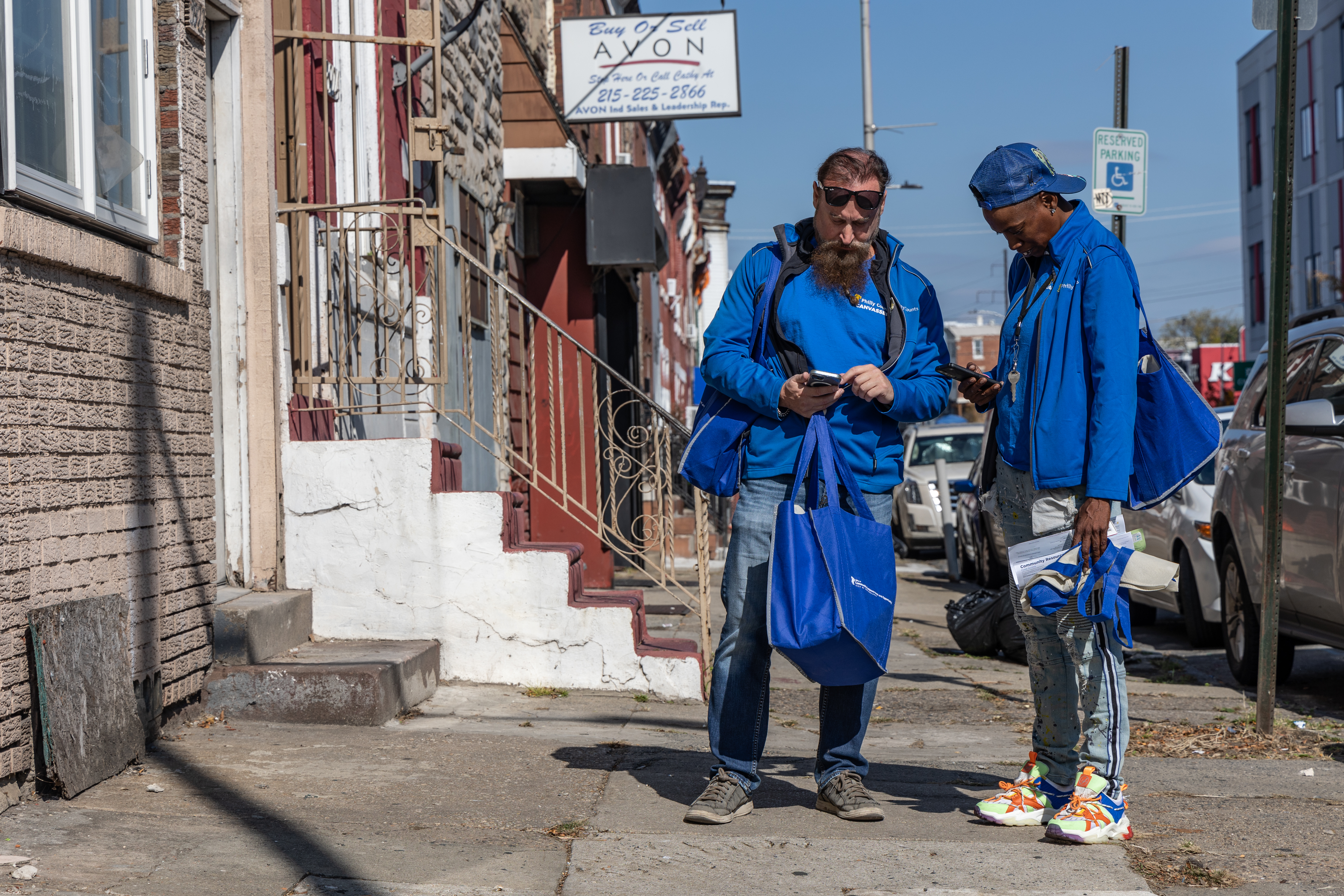 Dos personas con sudaderas azules a juego están paradas en una acera mirando sus teléfonos.