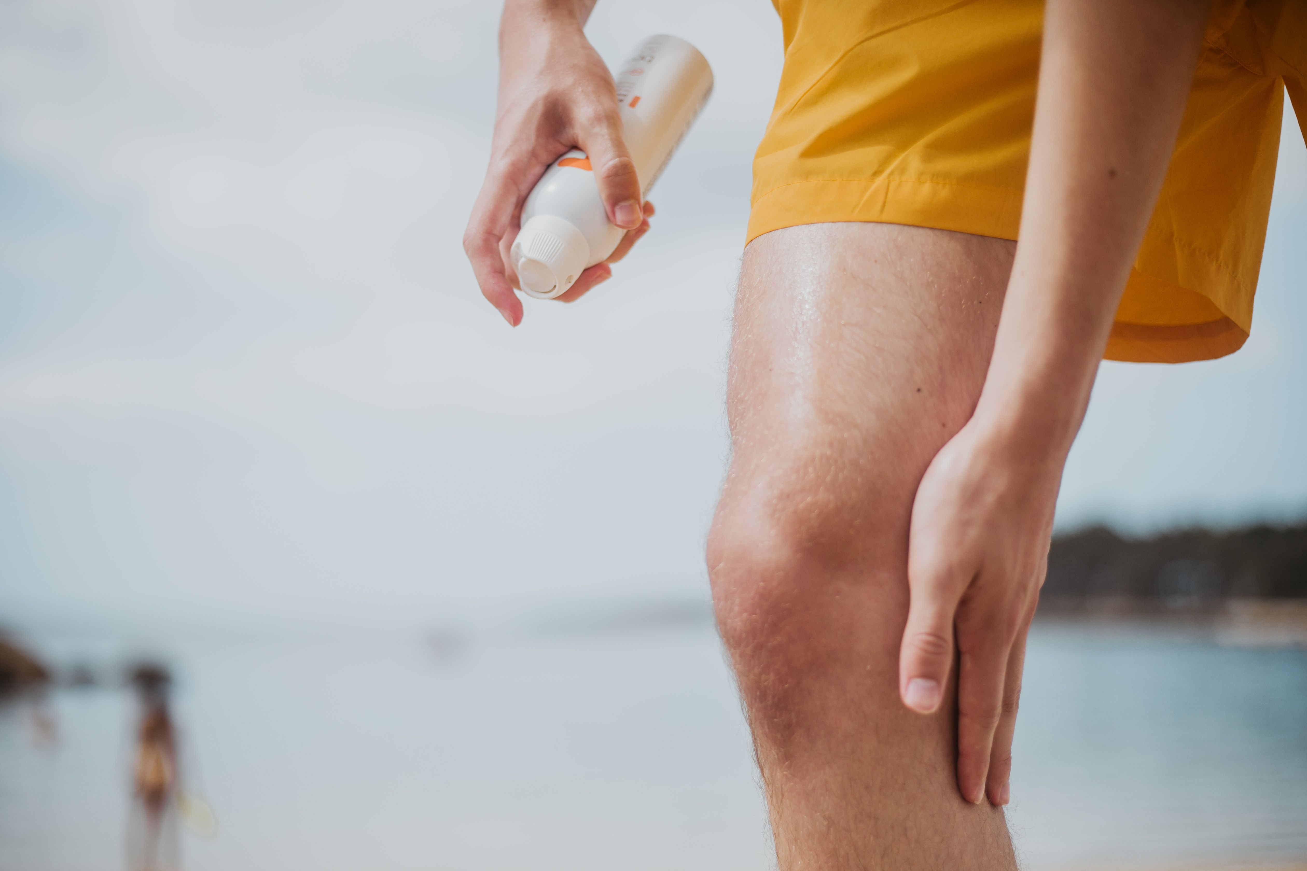 un hombre se rocía la pierna con protector solar en aerosol en la playa