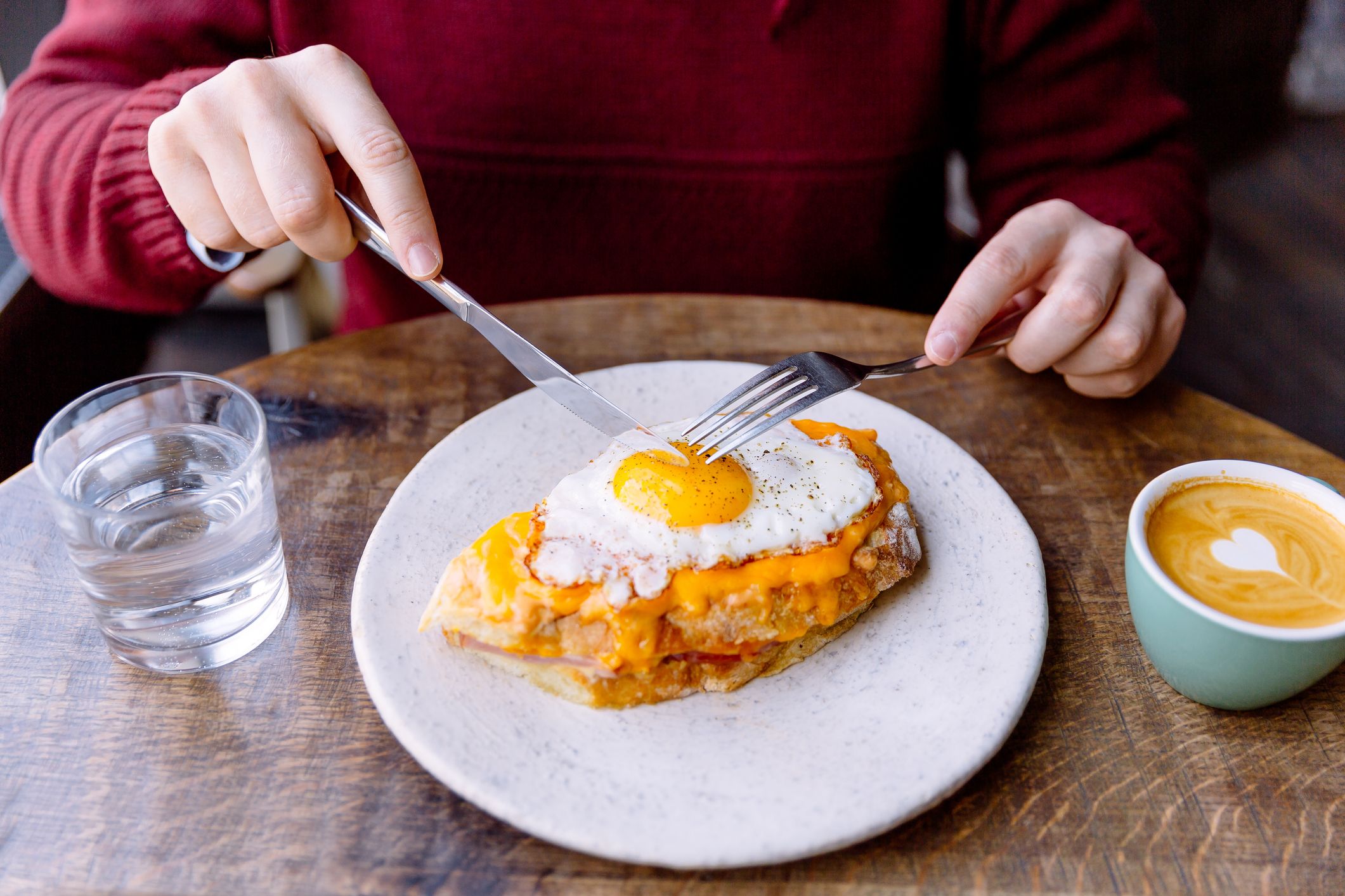 Hombre comiendo sándwich croque madame con queso y huevo frito