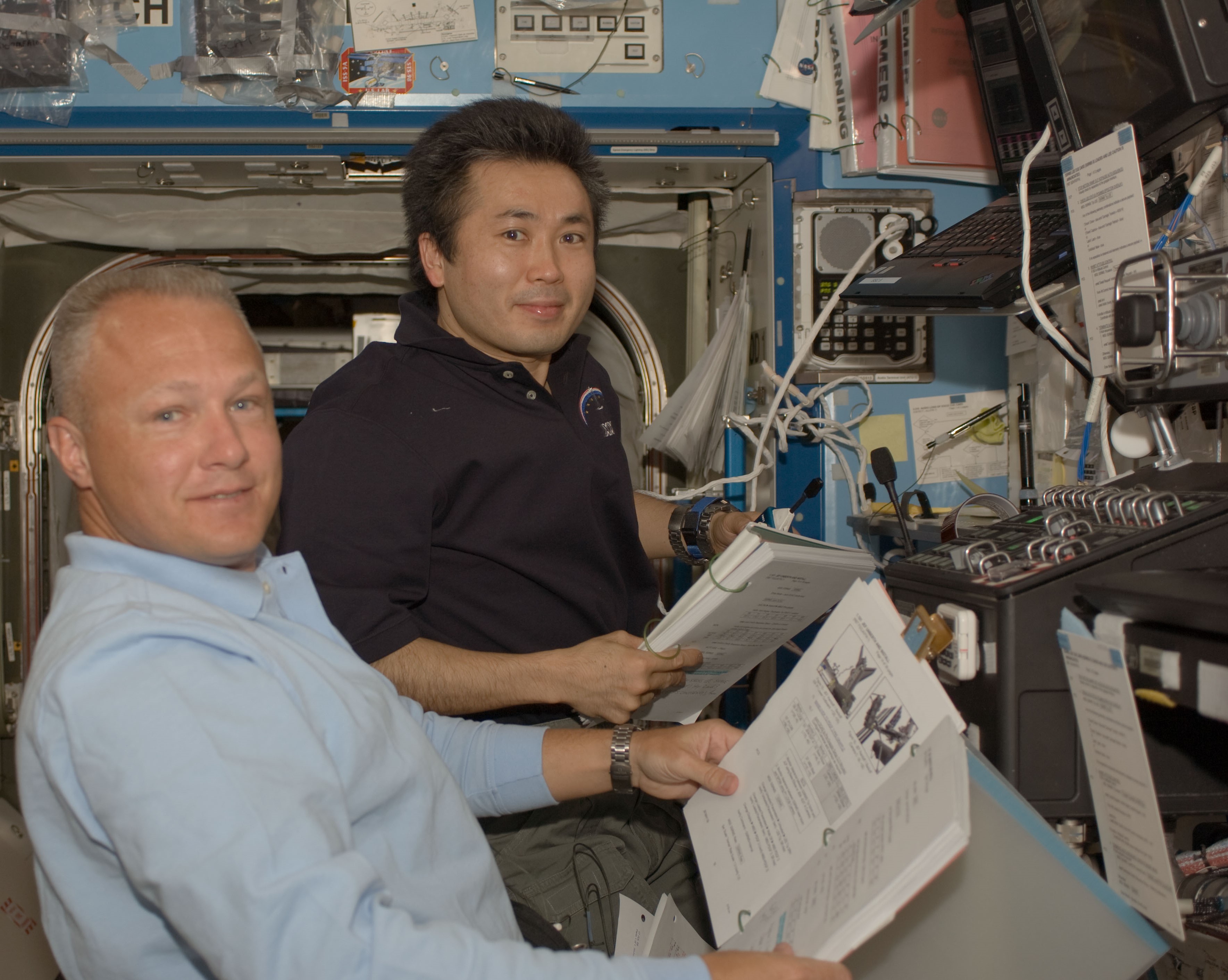 Douglas G. Hurley, a la izquierda, y Koichi Wakata, de la Agencia de Exploración Aeroespacial de Japón, operan el brazo robótico de la estación durante la primera caminata espacial.