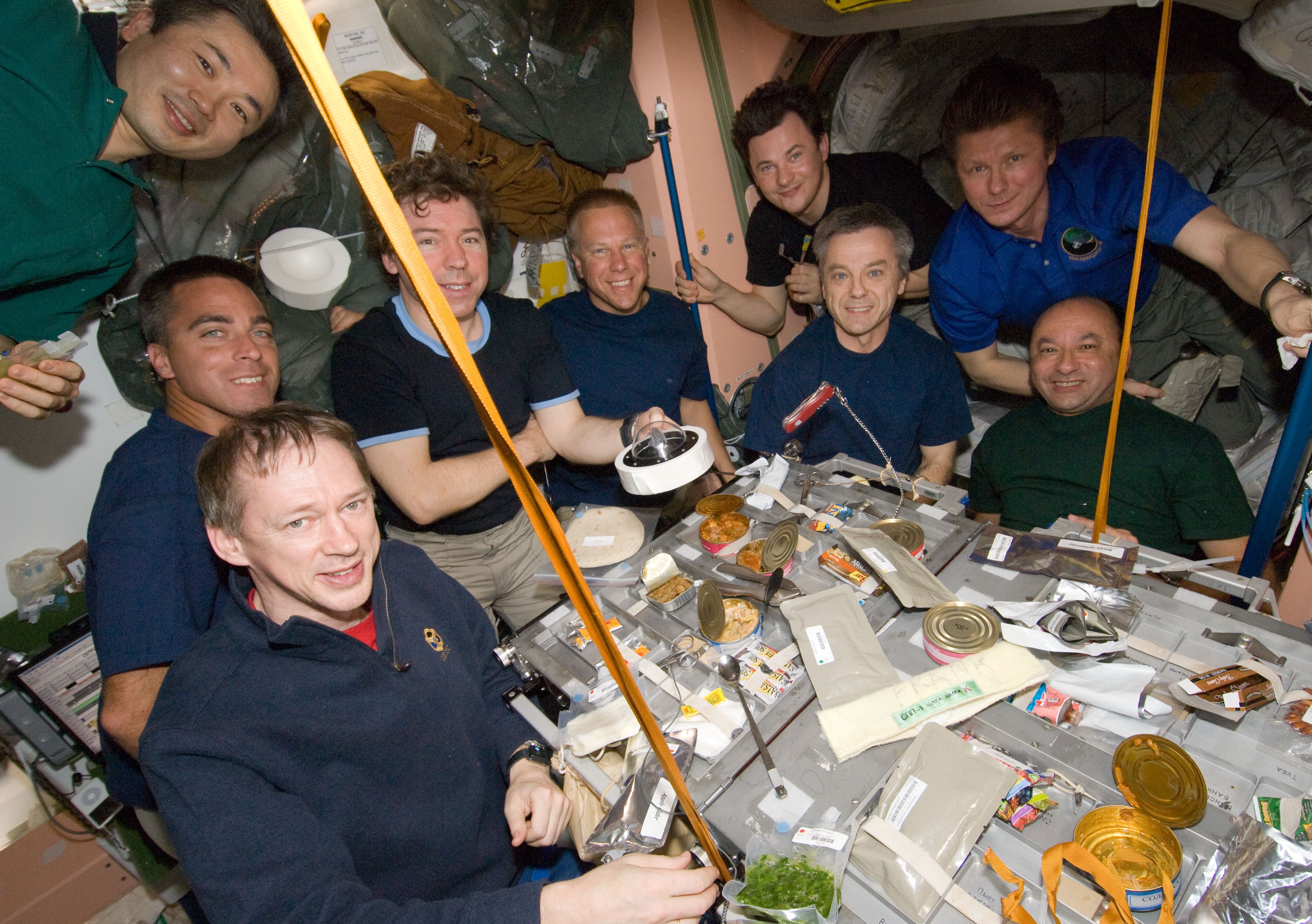 Nueve de los 13 miembros de la tripulación de la Expedición 20 y STS-127 comparten una comida, mientras el astronauta de la NASA Michael R. Barratt sostiene la roca lunar del Apolo 11